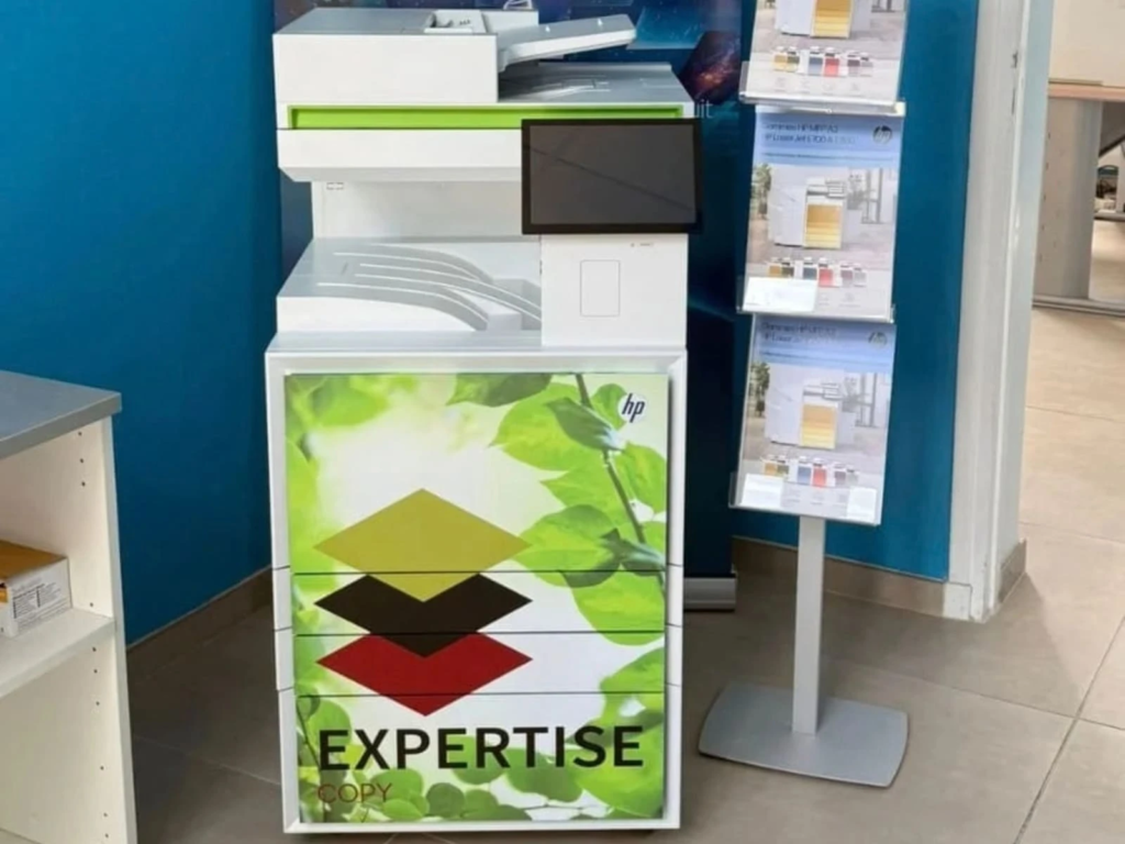 Photocopieur HP habillé d'un visuel vert personnalisé au logo Expertise Copy, dans un showroom