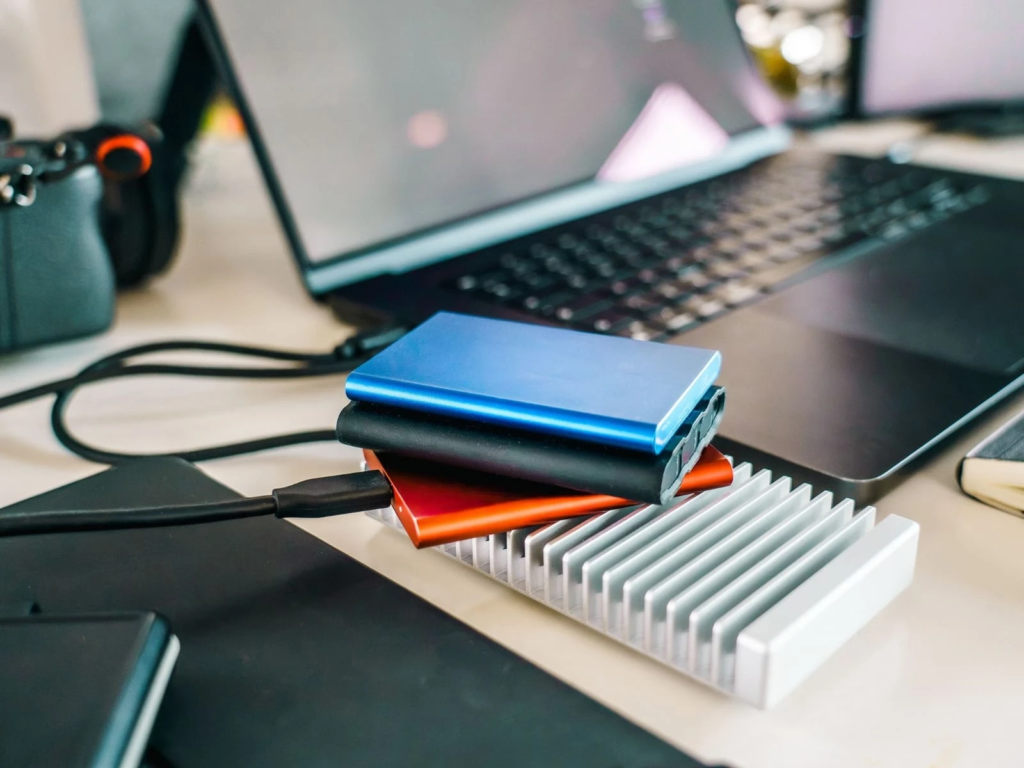 Trois disques durs externes empilés sur un bureau, à côté d'un ordinateur portable, reliés par un câble USB
